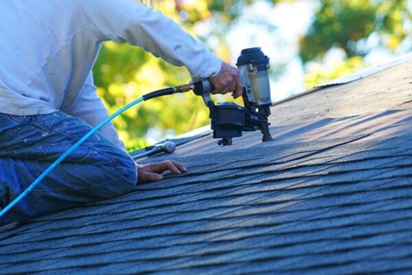handyman using nail gun to install shingle to repair roof